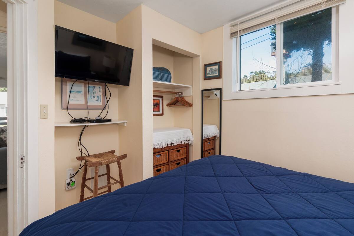 A bedroom with a bed, a television mounted on the wall, a window with a view, and a small stool.