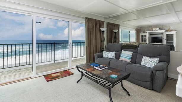A living room with a balcony overlooking the ocean, a gray sofa, a coffee table, and a television set. - Ocean Terrace Condominiums (Lincoln City)