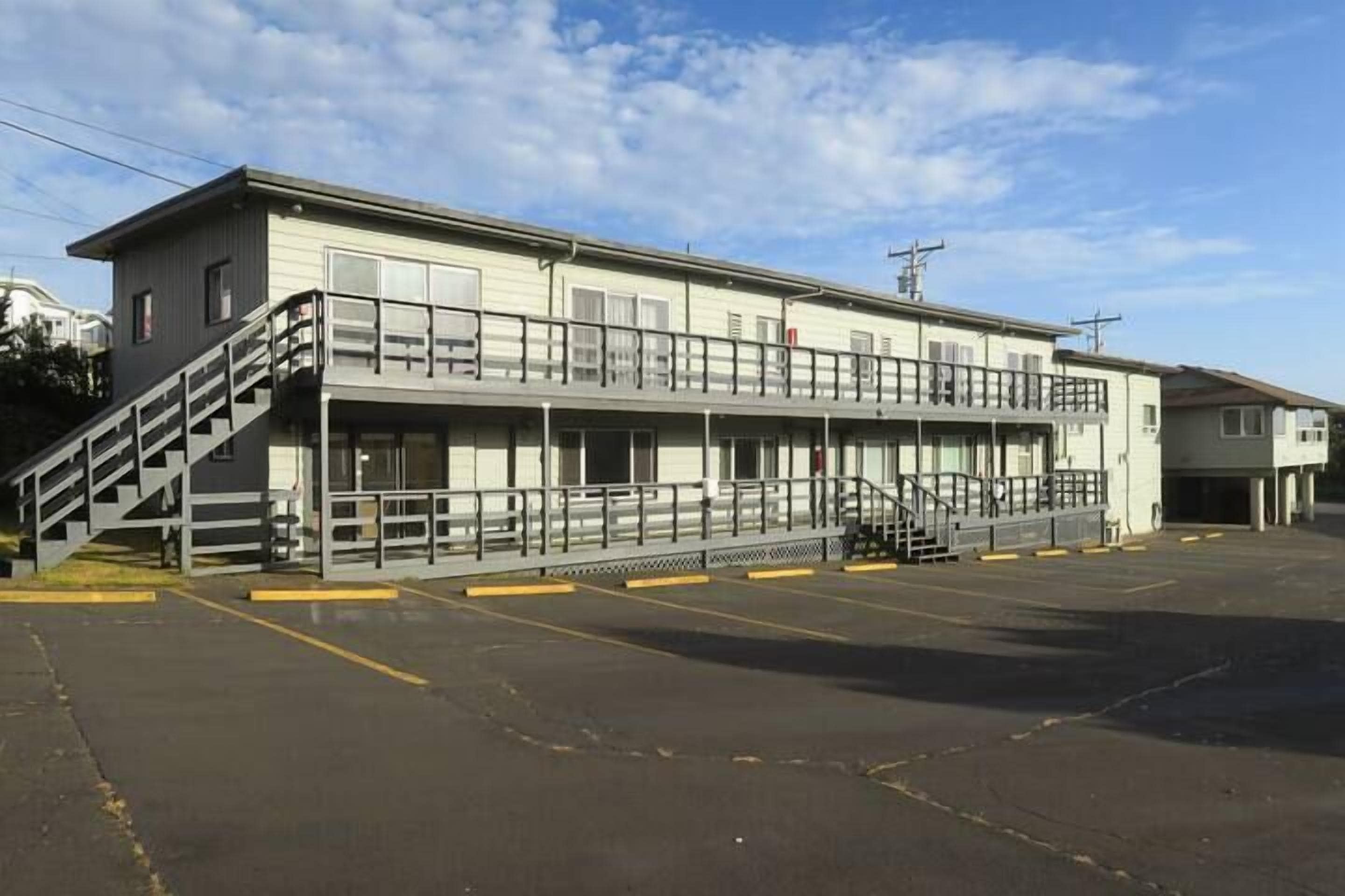 A two-story motel with a central staircase, a covered walkway, and a parking lot.