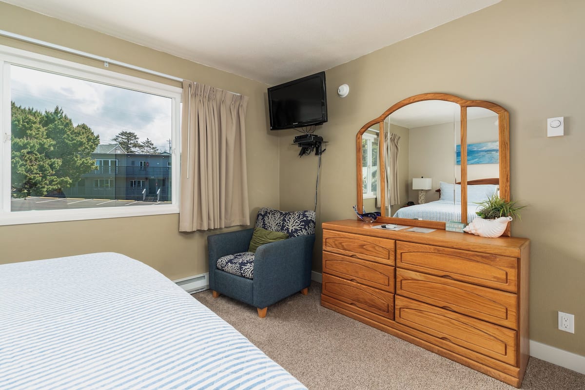A bedroom with a bed, a dresser, a chair, a TV, and a window with curtains.
