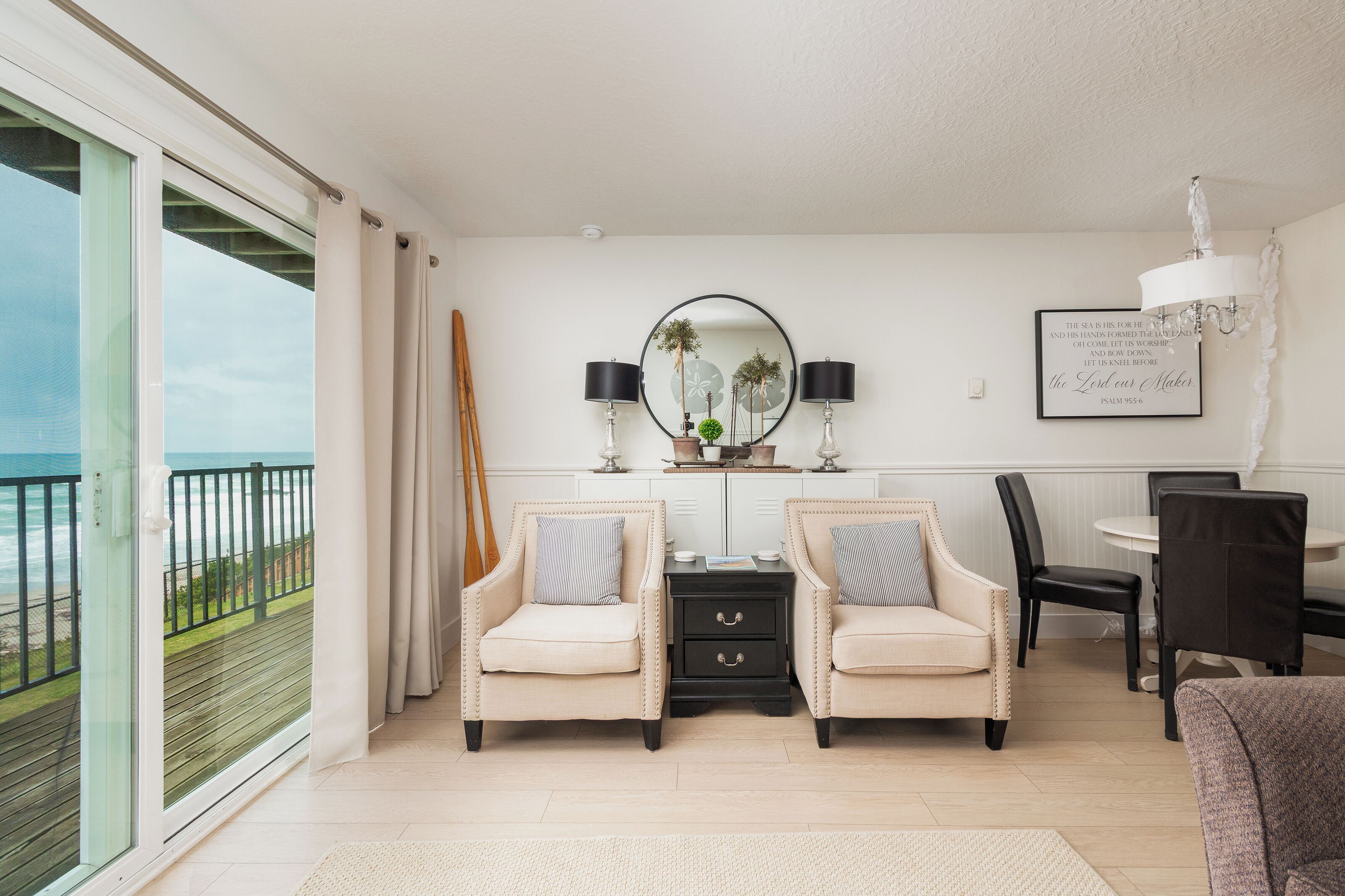 A room with two armchairs, a small table, a mirror, and a view of the ocean.