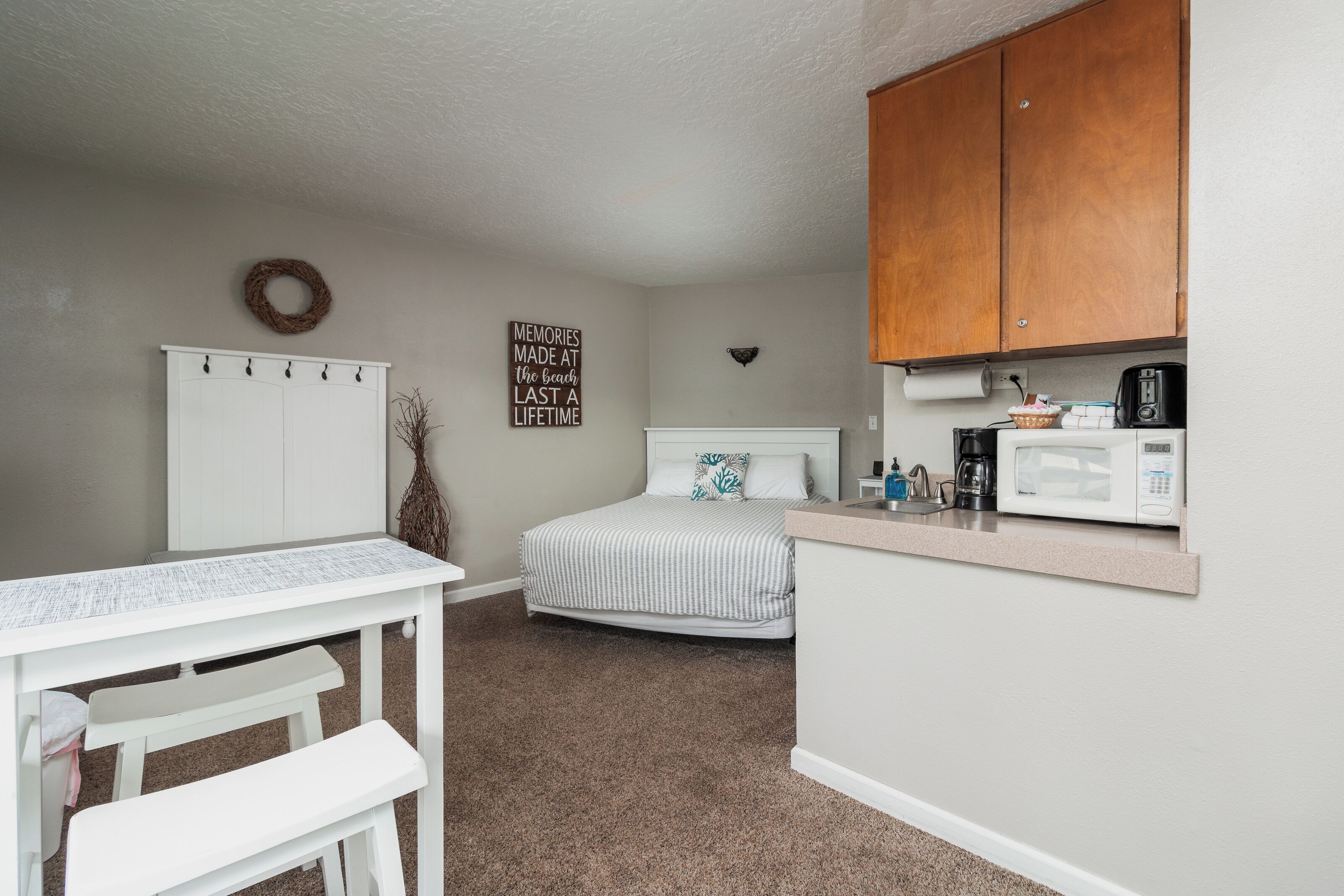Une chambre compacte comprenant un lit, un petit bureau et un coin cuisine.