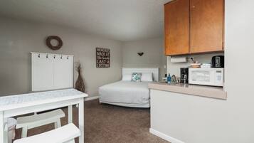 A compact bedroom with a bed, a small desk, and a kitchenette area.