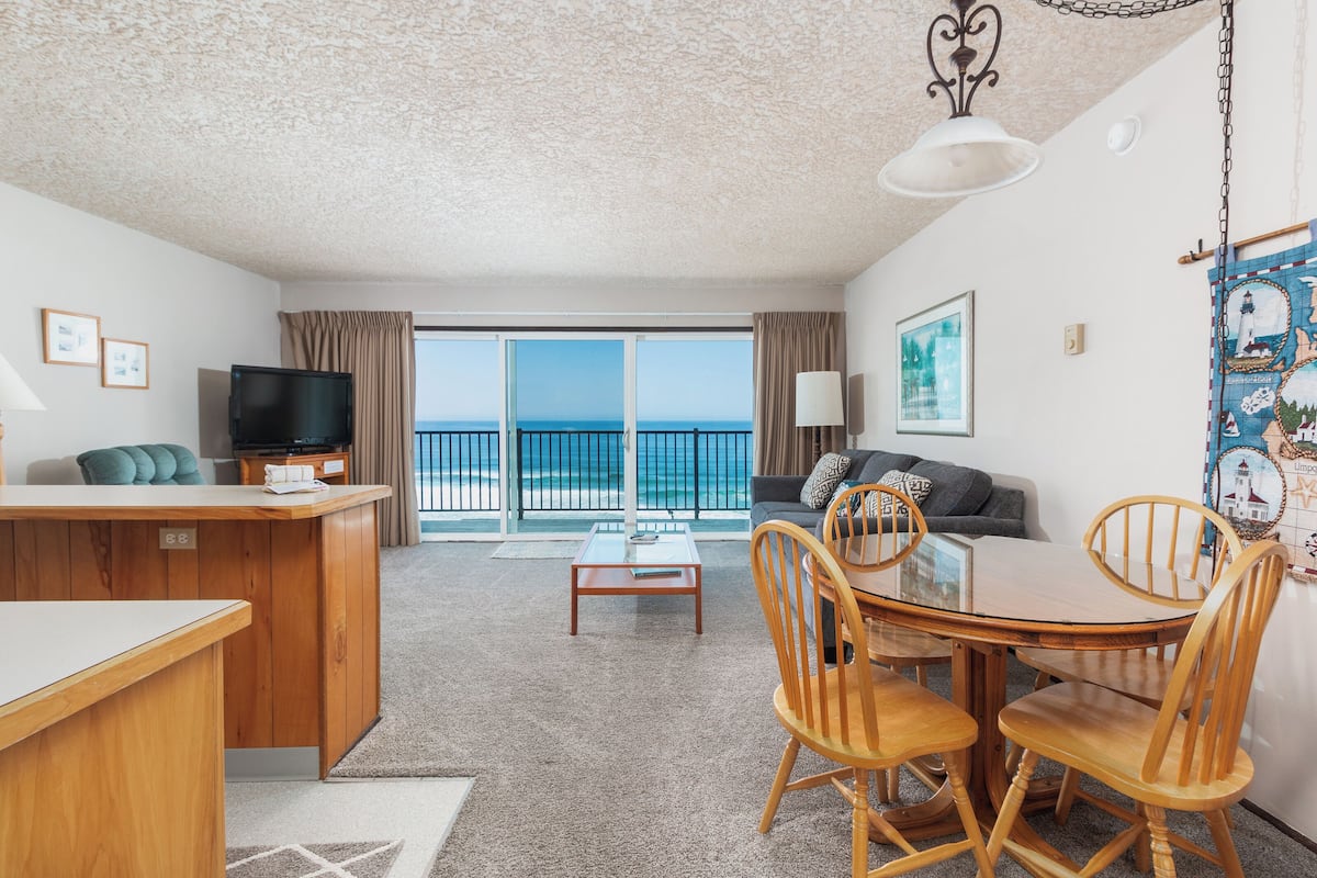 A spacious living area with a balcony, a wooden dining table, and a television.