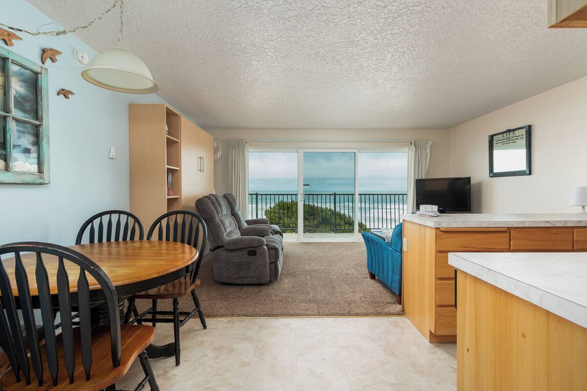 A cozy room with a dining table, chairs, a sofa, a TV, and a balcony with a view.