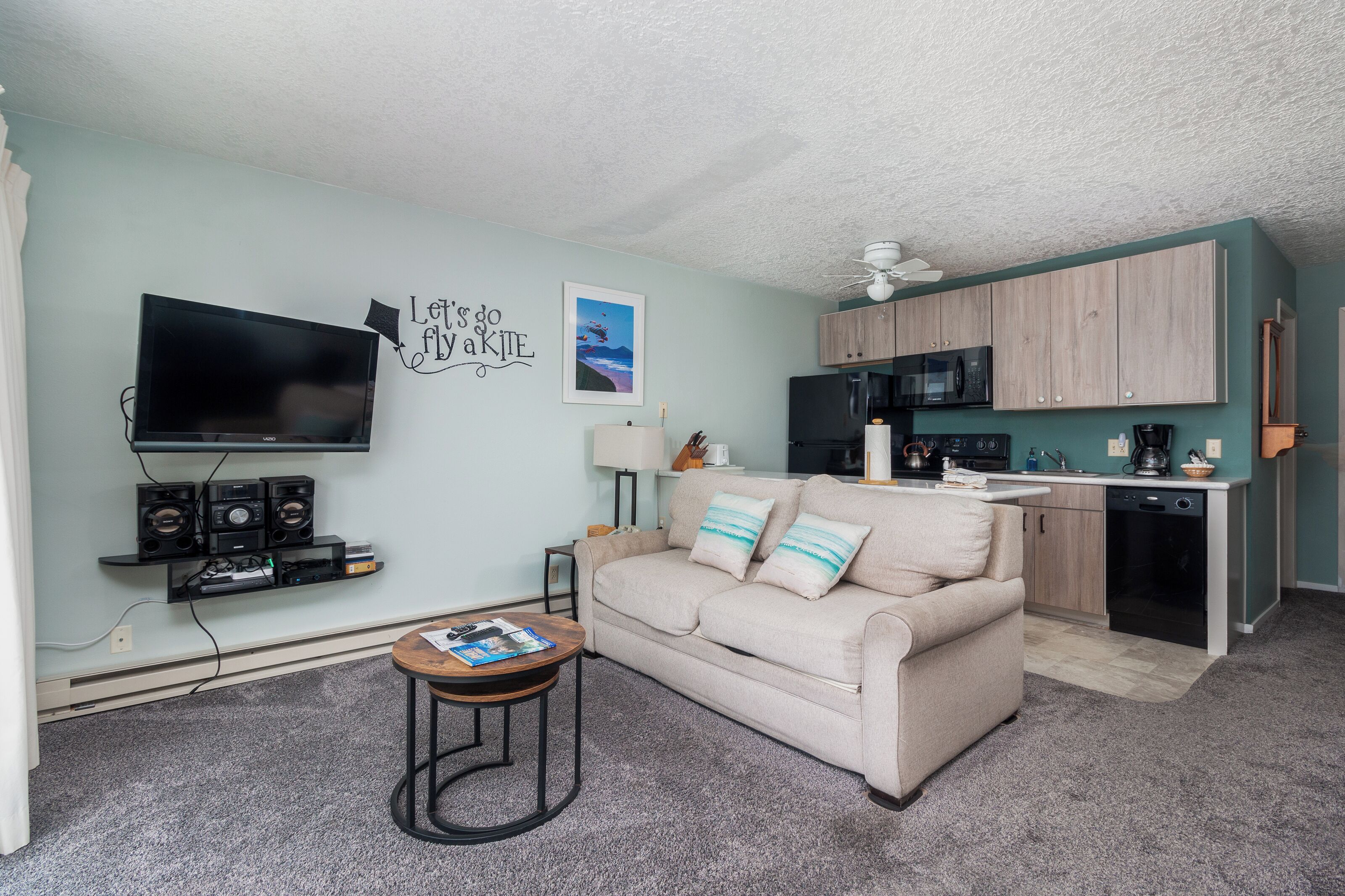 A compact living space with a kitchenette, a flat-screen TV, a sofa with cushions, and a small coffee table.