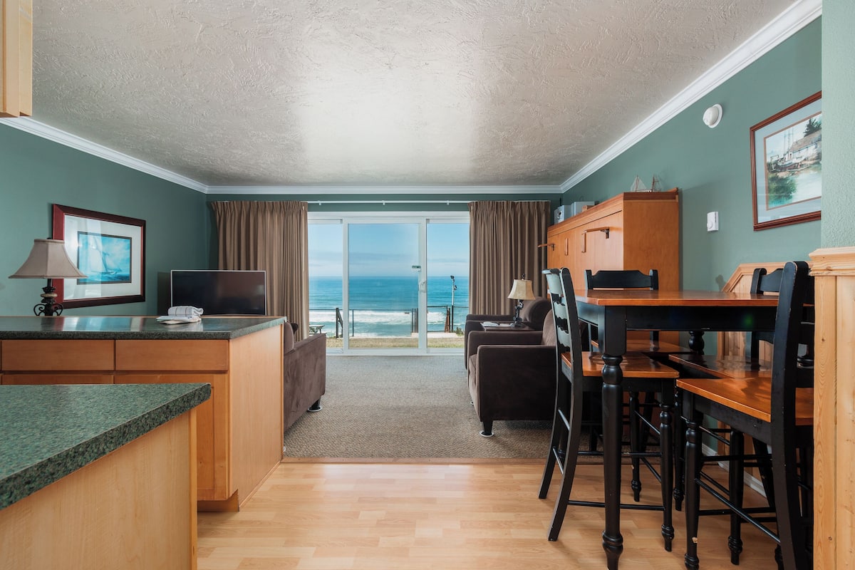 A compact room with a kitchen area, a dining table, and a view of the ocean.
