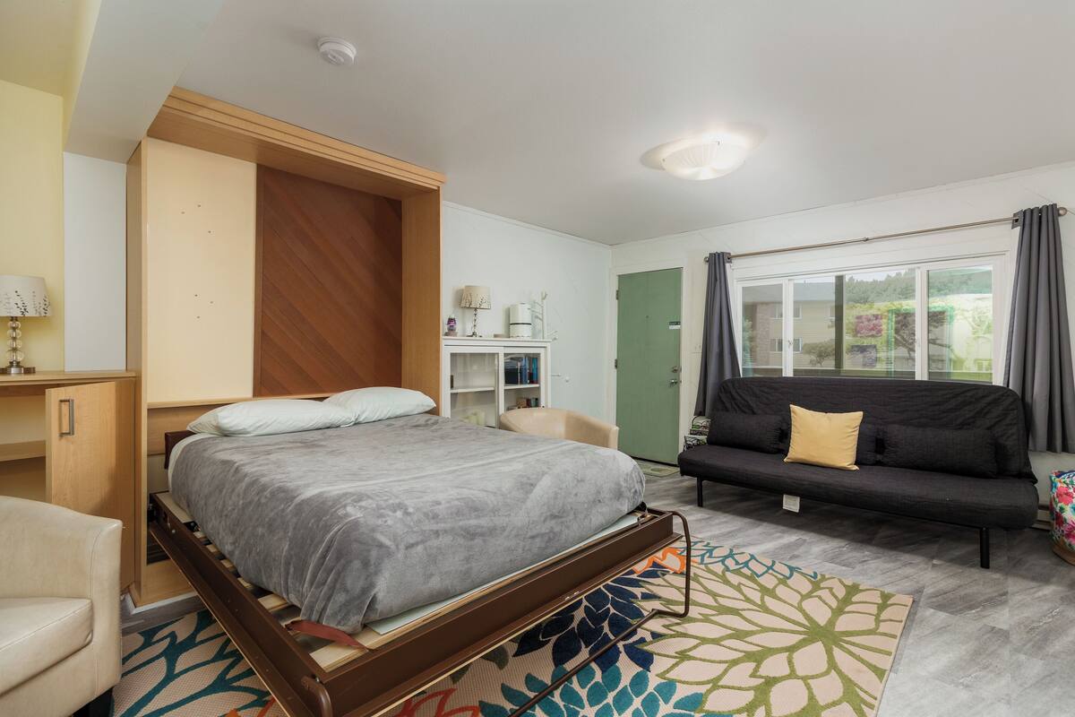 A bedroom with a bed, a sofa, a desk, and a window with curtains.