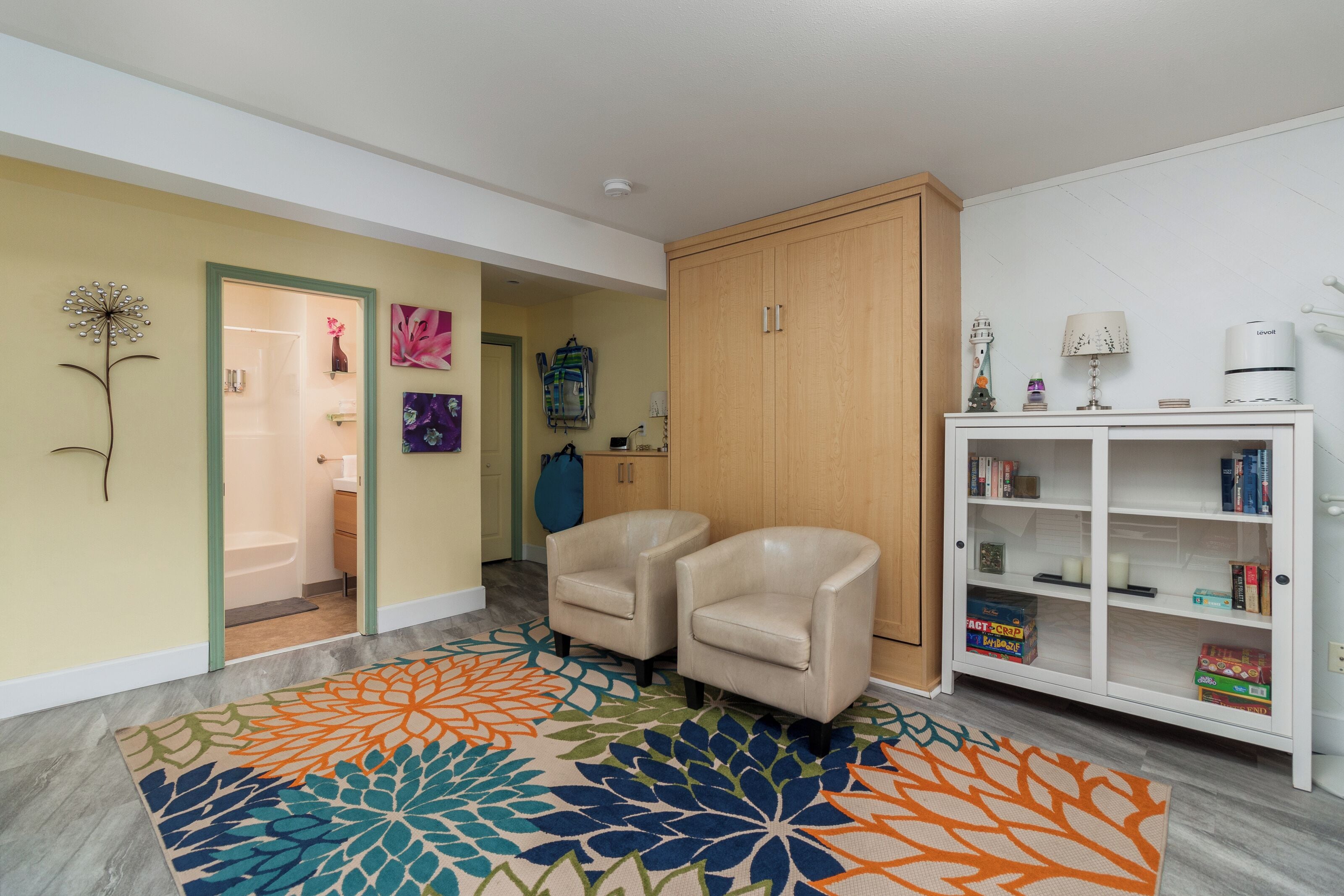 A living room with a colorful rug, a bookshelf, and a door leading to a bathroom.