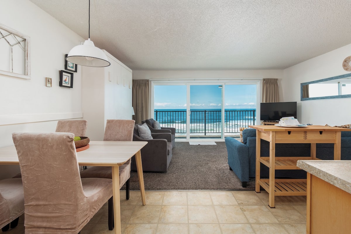 A modern living room with a dining area, a TV, and a balcony with a view of the sea.