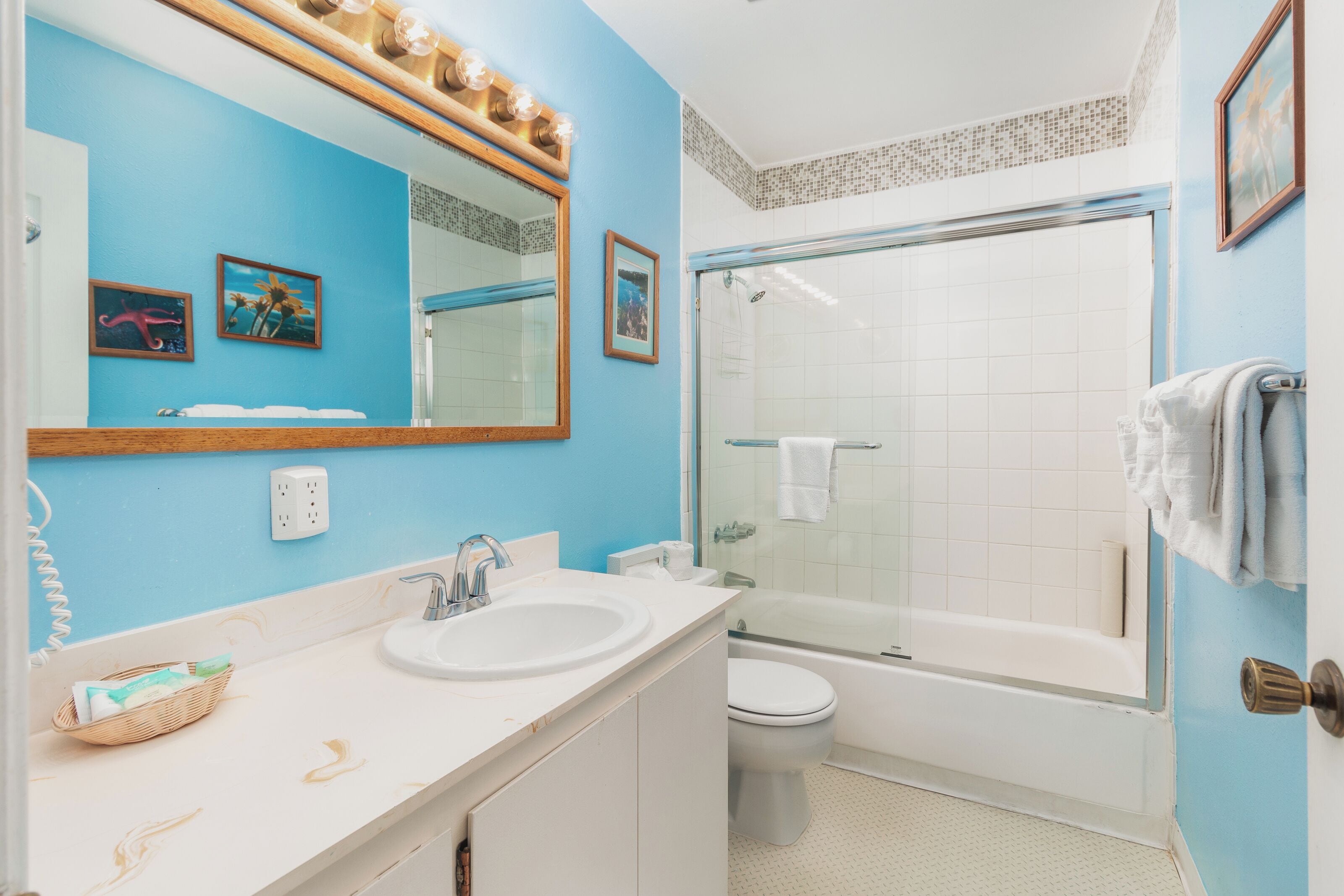 A bathroom with a sink, toilet, and bathtub. There is a shower with a glass door, a mirror above the sink, and a wall-mounted light fixture.