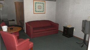A small, furnished room with a red sofa, a wooden chair, a small table, a television, and a cabinet. - Tidewater Motel (Hayes)
