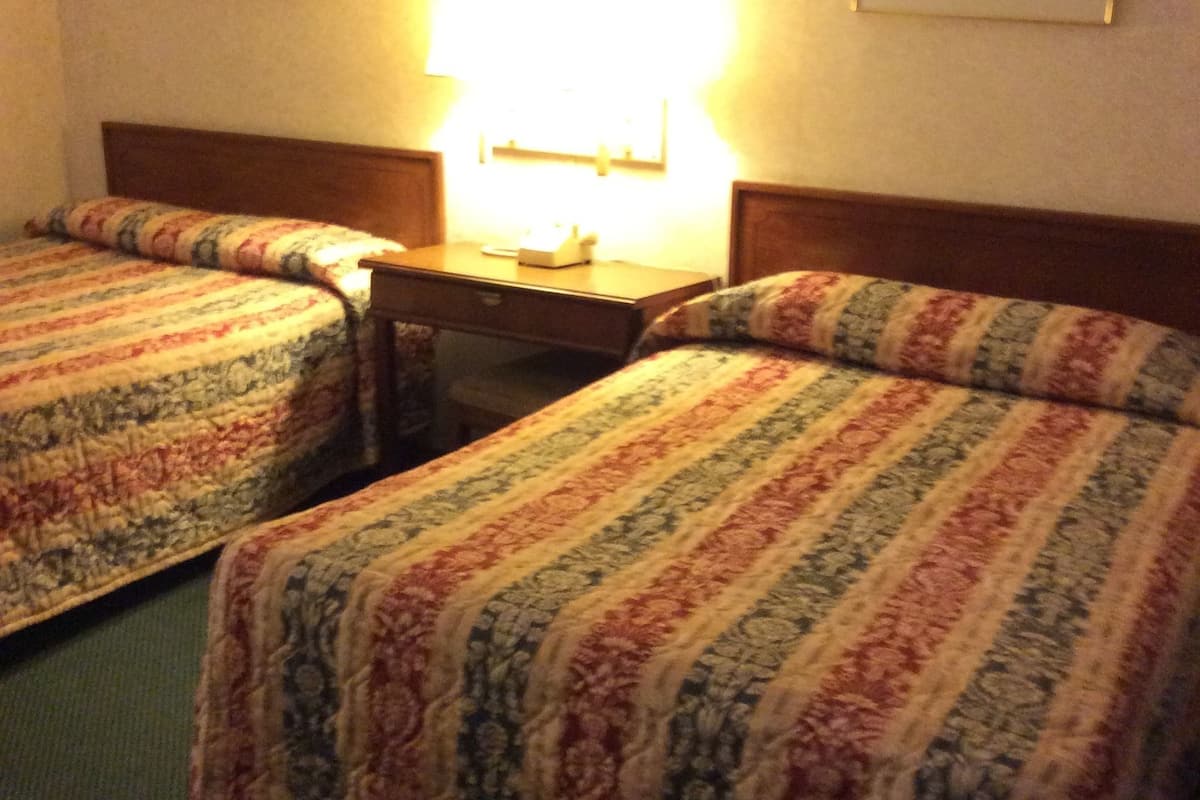 Quarto de hotel com duas camas de solteiro, uma mesa de cabeceira e uma luminária.
