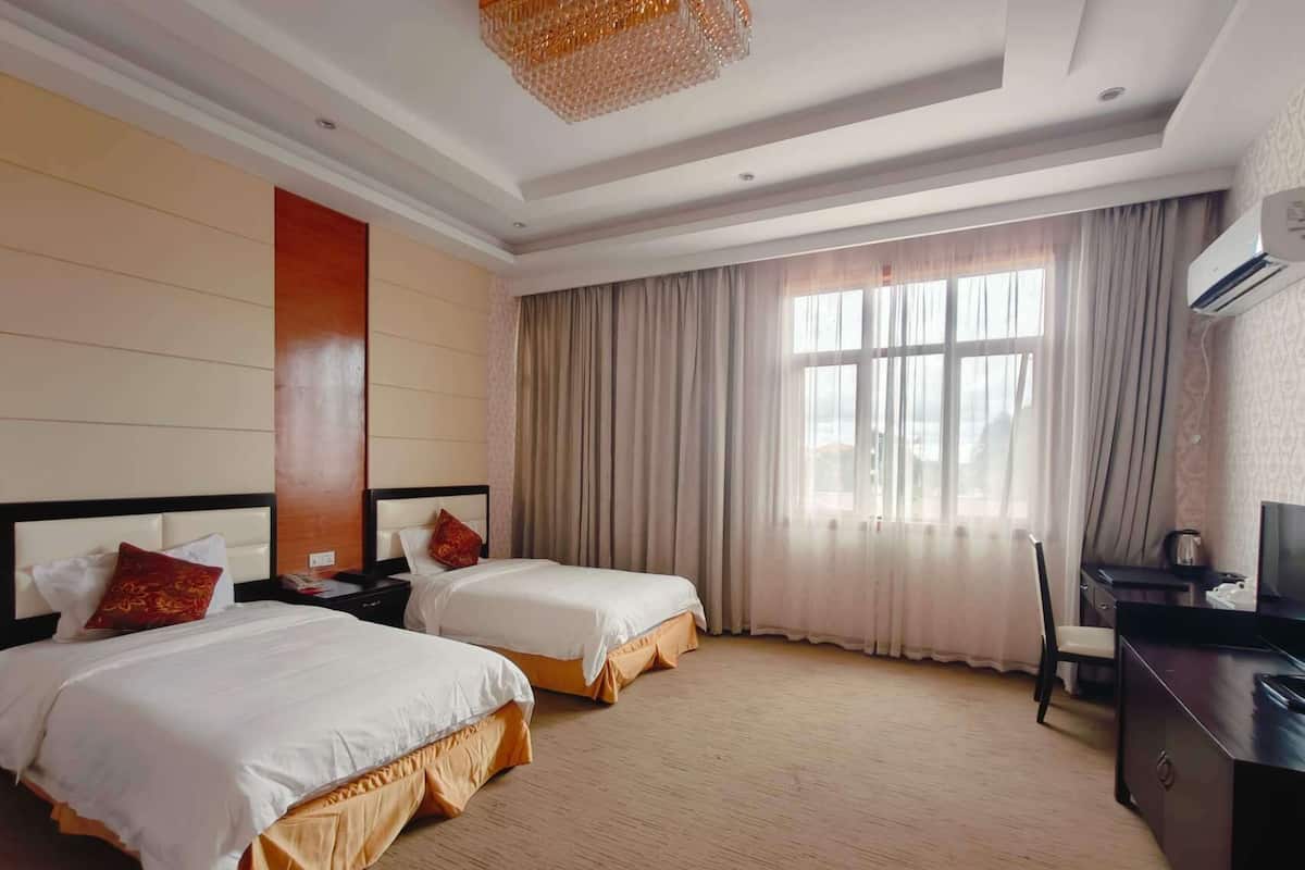 Habitación de hotel con dos camas, un escritorio, una silla, un televisor y un ventanal con cortinas.