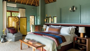 A bedroom with a large bed, bedside tables, a chair, and a small table with books. - Tamodi Lodge and Stables (Keurboomstrand)