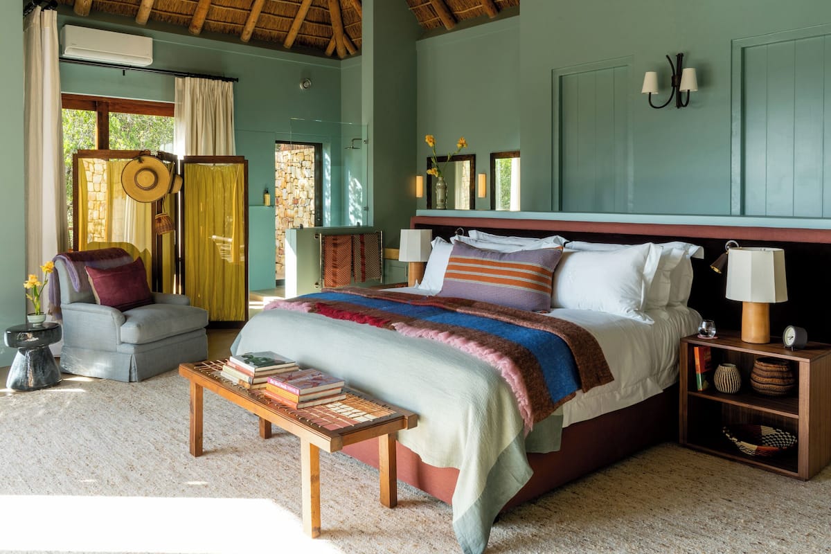 Une chambre à coucher avec un grand lit, des tables de chevet, une chaise et une petite table avec des livres.