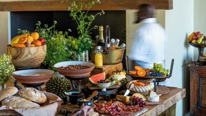 A breakfast buffet with various foods and drinks, a painting on the wall, and a chef in motion. - Tamodi Lodge and Stables (Keurboomstrand)