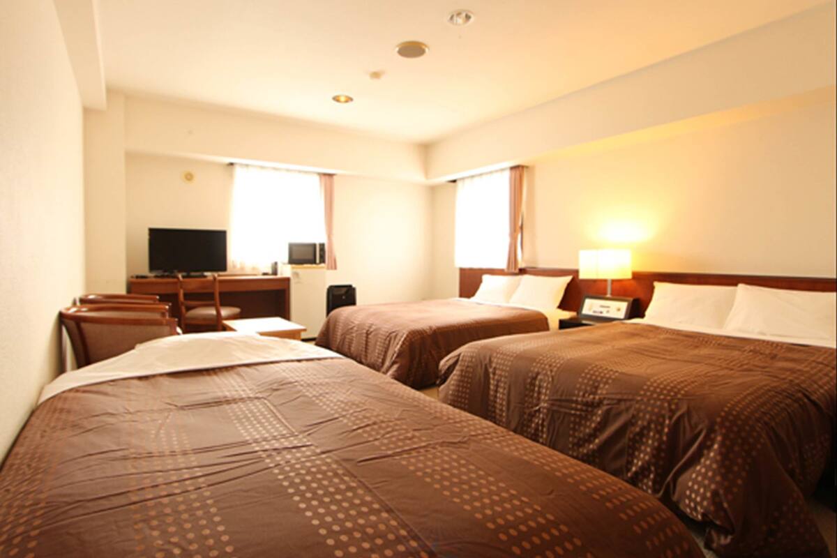 Habitación de hotel con dos camas, un escritorio con computadora, un televisor y una ventana con cortinas.