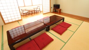A tatami mat room with a low wooden table, red cushions, a TV, and sliding doors. - Hotel Livemax Chitose (Chitose)