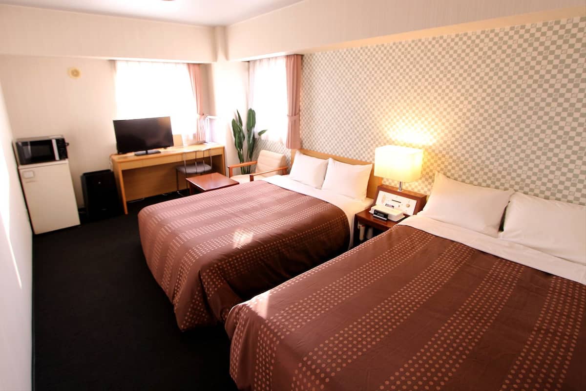 Habitación de hotel con dos camas, un escritorio, televisión, refrigerador pequeño y una lámpara.