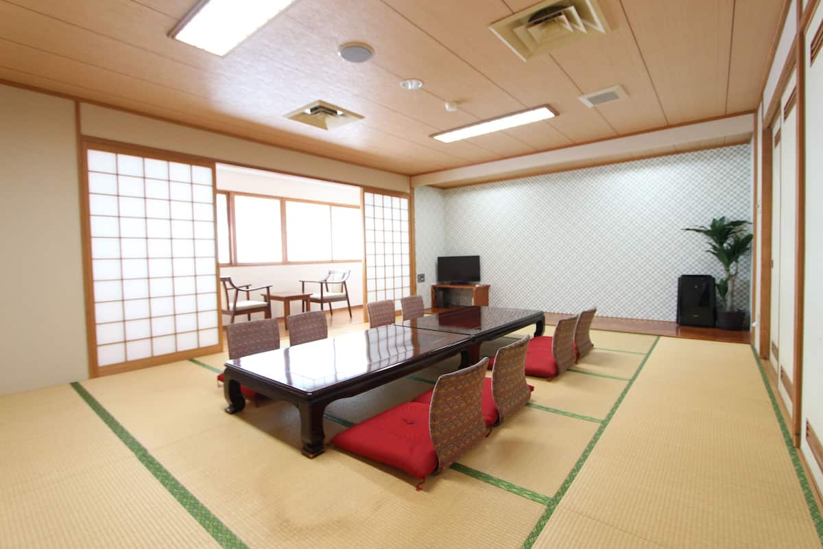 Una habitación tradicional japonesa con suelo de tatami, una mesa baja con cojines y puertas correderas.