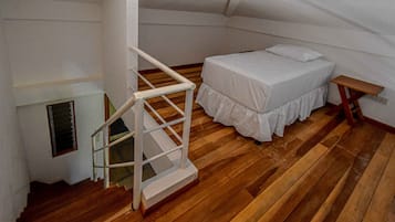 Un dormitorio con piso de madera, una cama blanca con cubrecama blanco, una mesita de noche blanca y una escalera blanca.