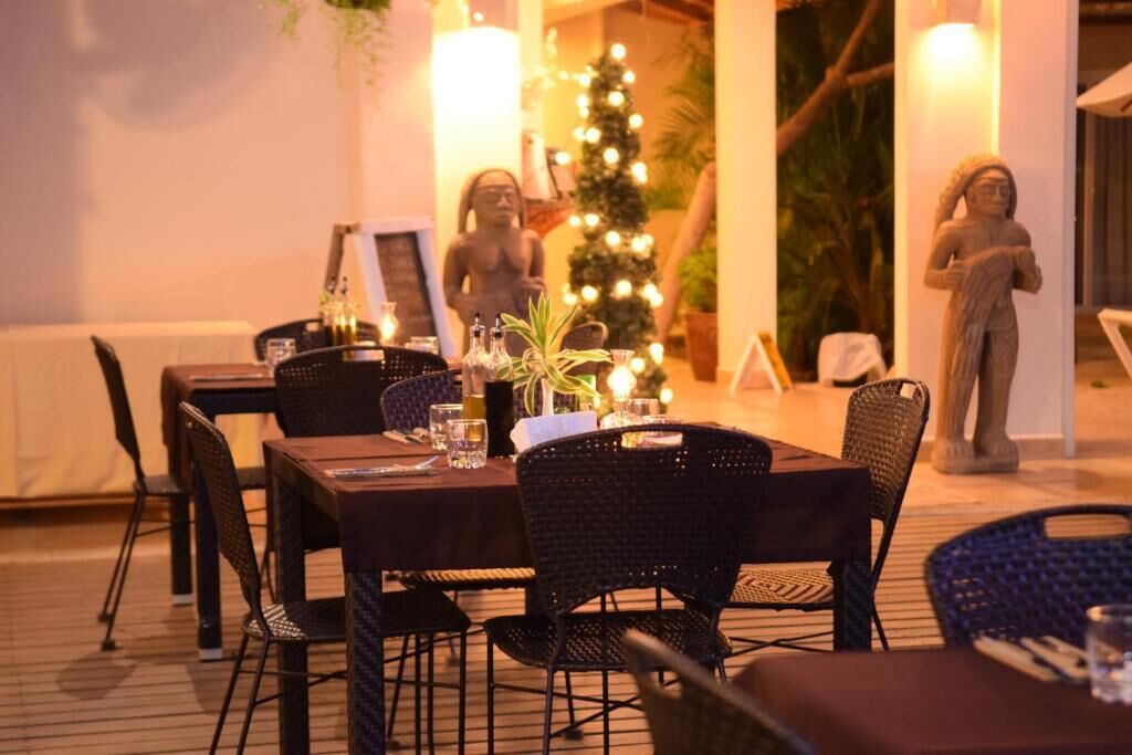 Ein Außenbereich mit Essbereich, Korbstühle und Tische, ein Weihnachtsbaum und Statuen im Hintergrund.