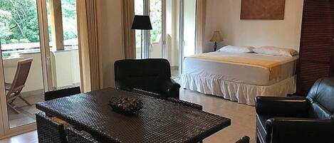 Una habitación con cama, una mesa de comedor con sillas, un sofá y un amplio ventanal con cortinas.