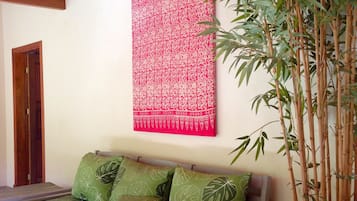 Una habitación con una cama, un tapiz rojo estampado y una planta de bambú.