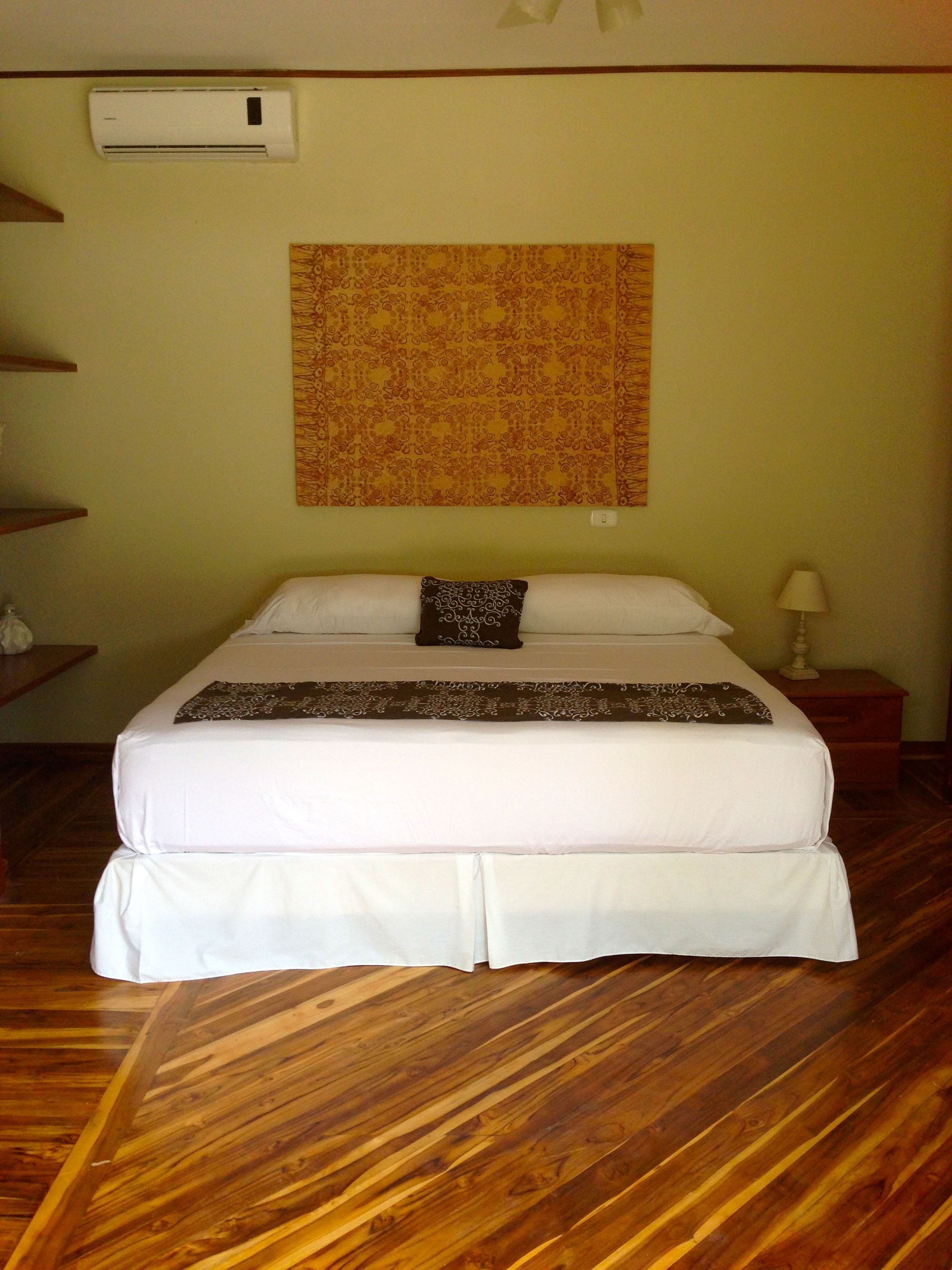 Una cama bien hecha con una colcha estampada, un aire acondicionado de pared y un tapiz decorativo.