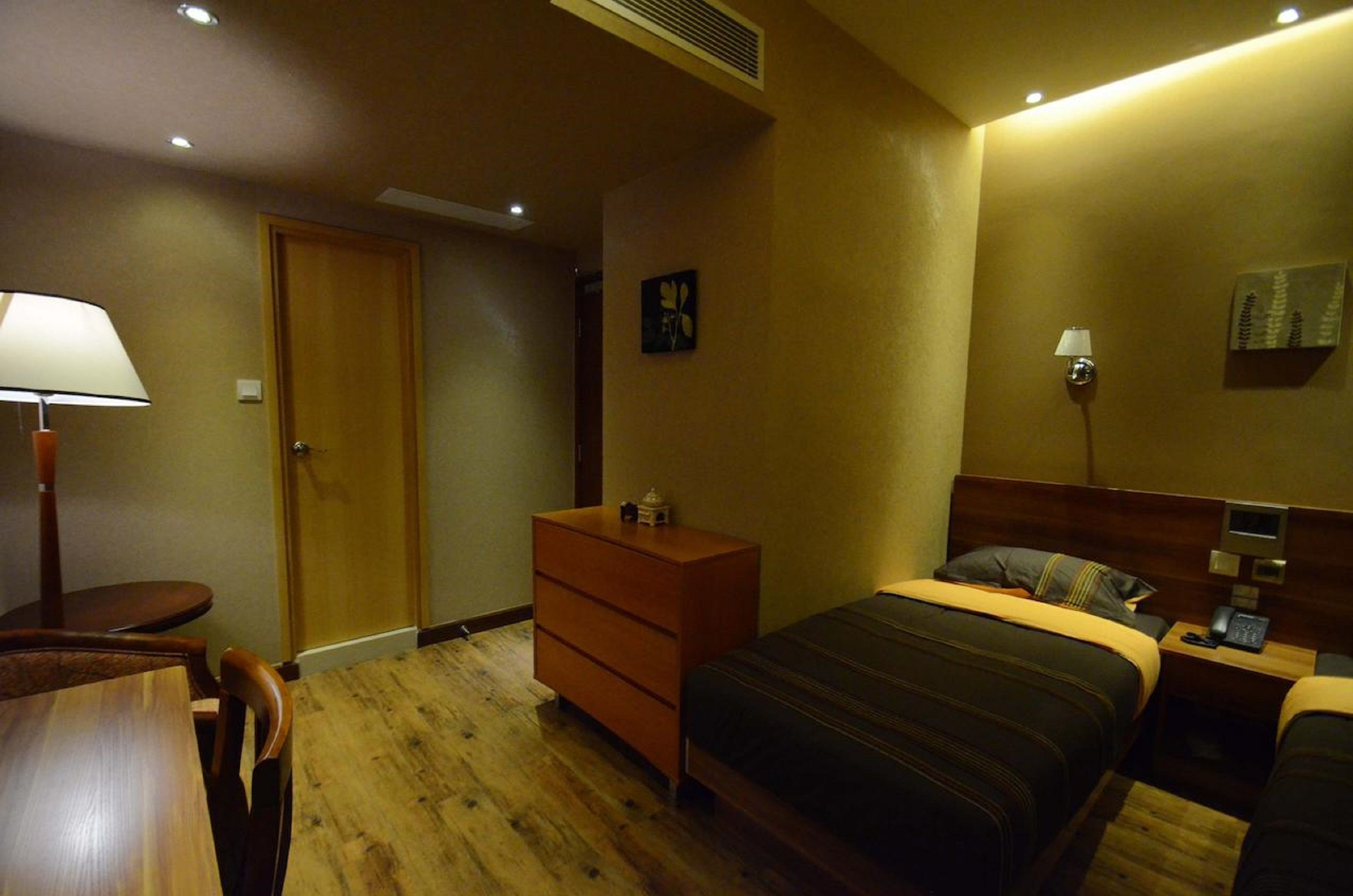 A hotel room with a bed, dresser, desk, chair, lamp, and artwork on the wall.