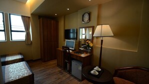 Une chambre d’hôtel avec un bureau en bois, une télévision, un petit réfrigérateur, une table à manger avec une lampe et deux lits.