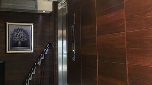 Un ascenseur moderne doté d’un écran numérique, d’un panneau indiquant qu’il est accessible aux personnes en fauteuil roulant, et d’un escalier muni d’une rampe.