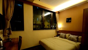 Une chambre d’hôtel équipée d’un lit, d’un bureau, d’une chaise, d’une fenêtre avec des rideaux et d’une lampe de chevet.