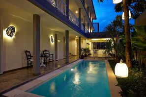 Una piscina amb terrassa coberta, mobiliari exterior i il·luminació decorativa a la paret.
