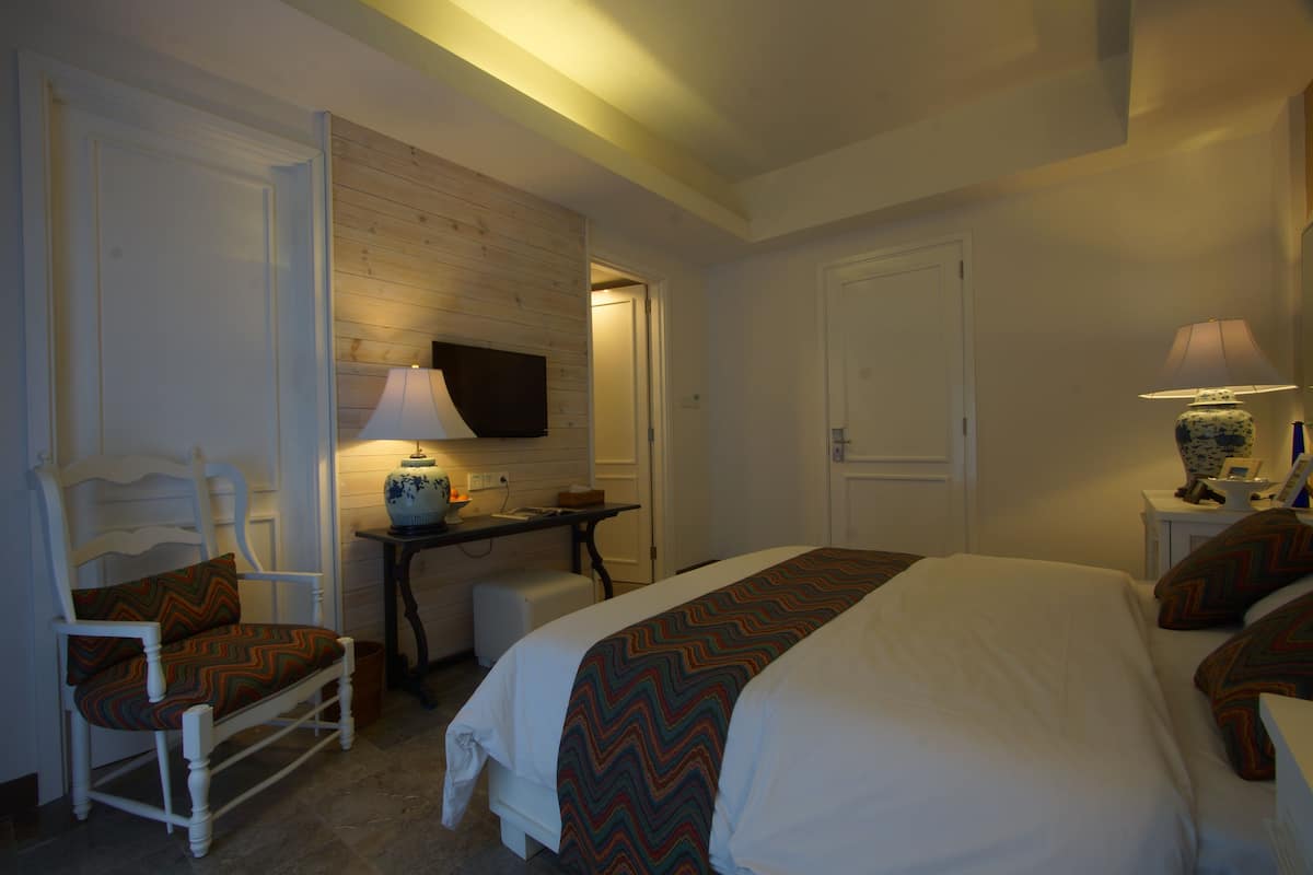 A hotel room with a bed, a chair, a desk, a television, and two lamps.