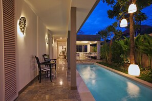 A swimming pool with a patio area, a dining table with chairs, and decorative wall lighting. - Summerhome (Keroboken Kelod)
