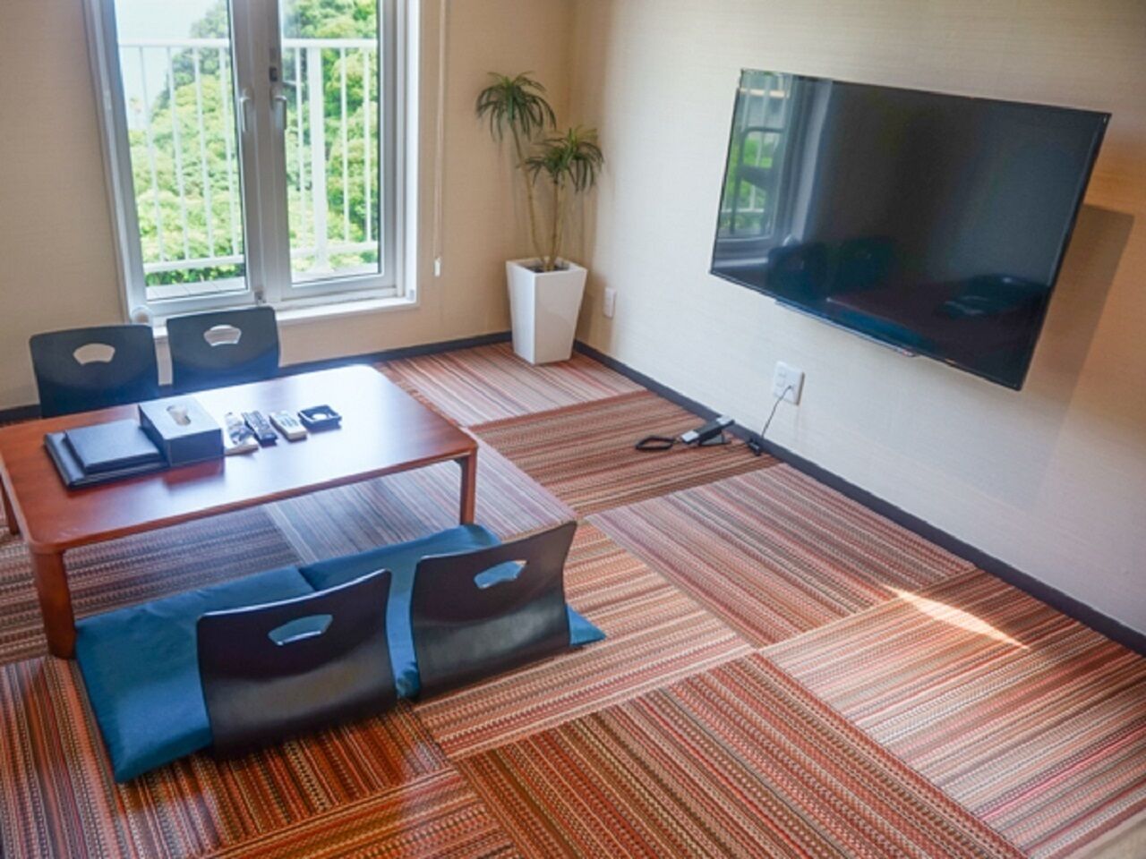 A conference room with a large table, chairs, a TV, and a potted plant.