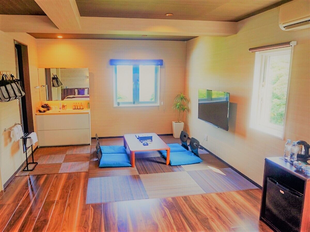 A compact room with a bed, a small table, a TV, and a kitchenette.