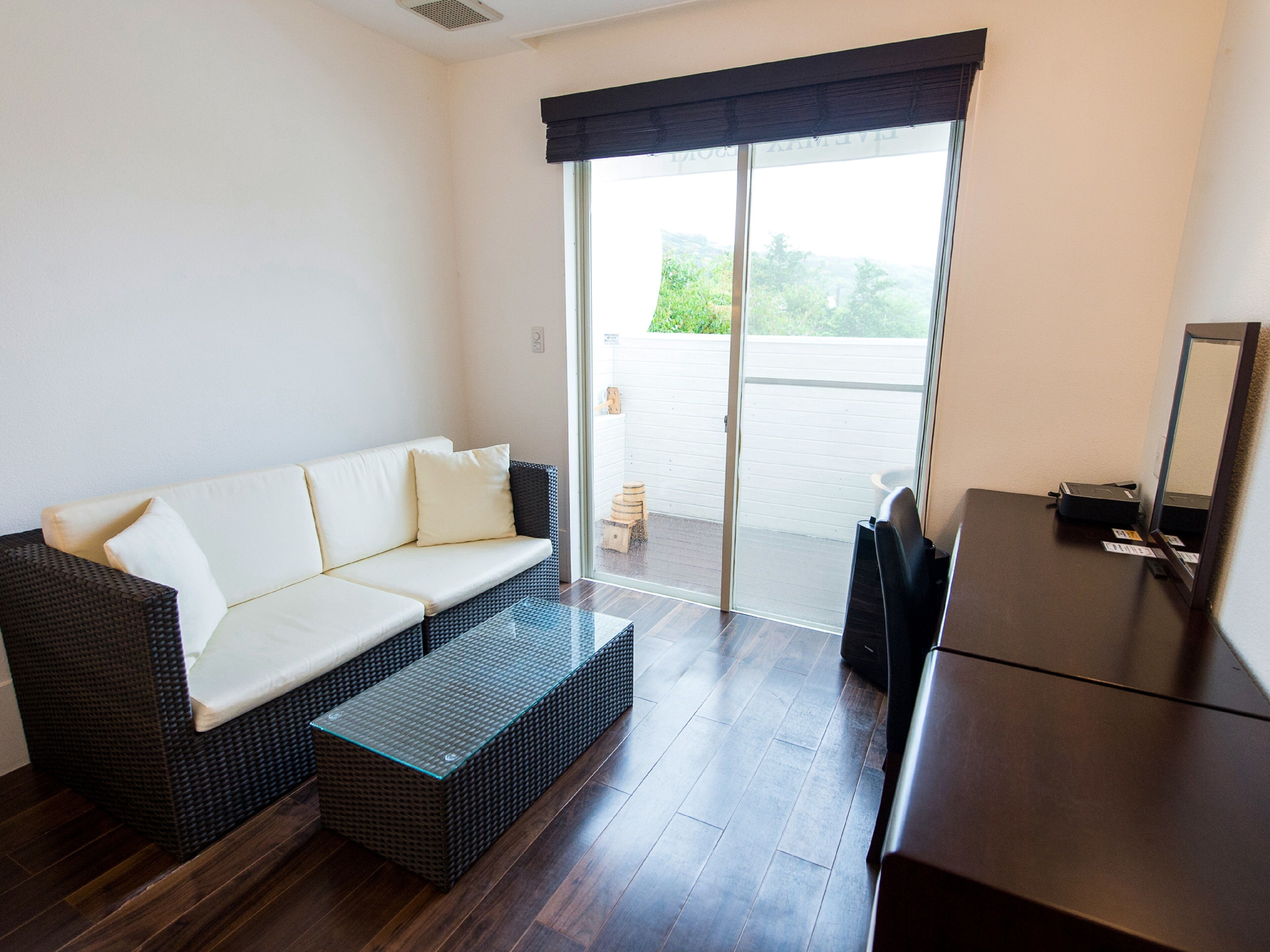 A room with a sofa, a small table, and a desk. There is a sliding glass door leading to an outdoor area.