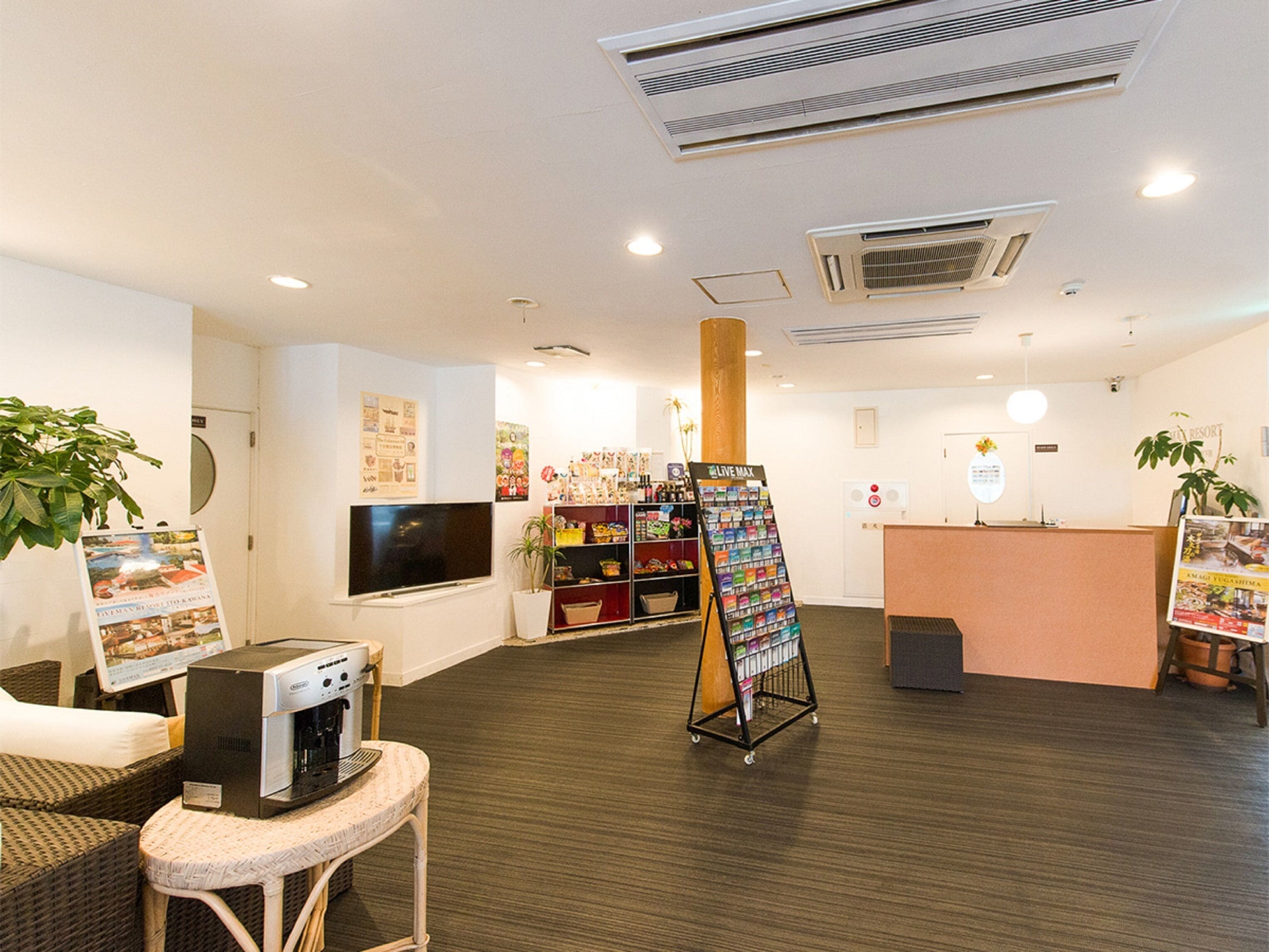 Zona de recepción con máquina de café, televisor, tablón de anuncios y mostrador de recepción.
