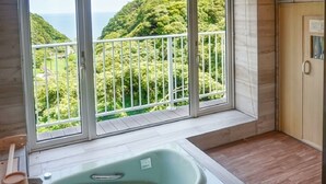 A bathroom with a bathtub, a wooden bench, a wooden cabinet, and a view of a lush green landscape through large windows. - LiVEMAX RESORT Izu Shimoda (Shimoda)