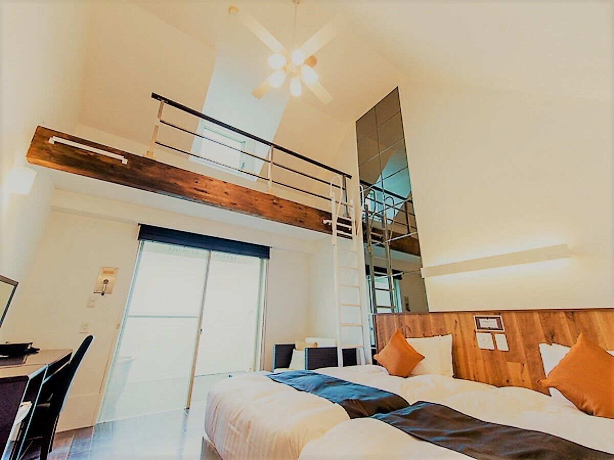 A room with a bunk bed, a desk, a chair, a ladder, and a large window.