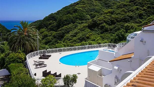 A pool area with lounge chairs, a swimming pool, and a view of a lush green hillside. - LiVEMAX RESORT Izu Shimoda (Shimoda)