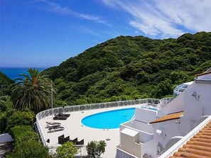 A pool area with lounge chairs, a swimming pool, and a view of a lush green hillside. - LiVEMAX RESORT Izu Shimoda (Shimoda)