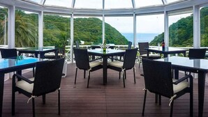 A covered outdoor dining area with tables and chairs, overlooking a lush green landscape and the sea. - LiVEMAX RESORT Izu Shimoda (Shimoda)