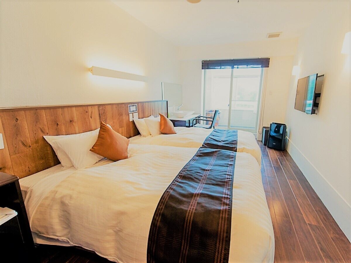 A hotel room with two beds, a wooden headboard, a large window, and a desk with a chair.
