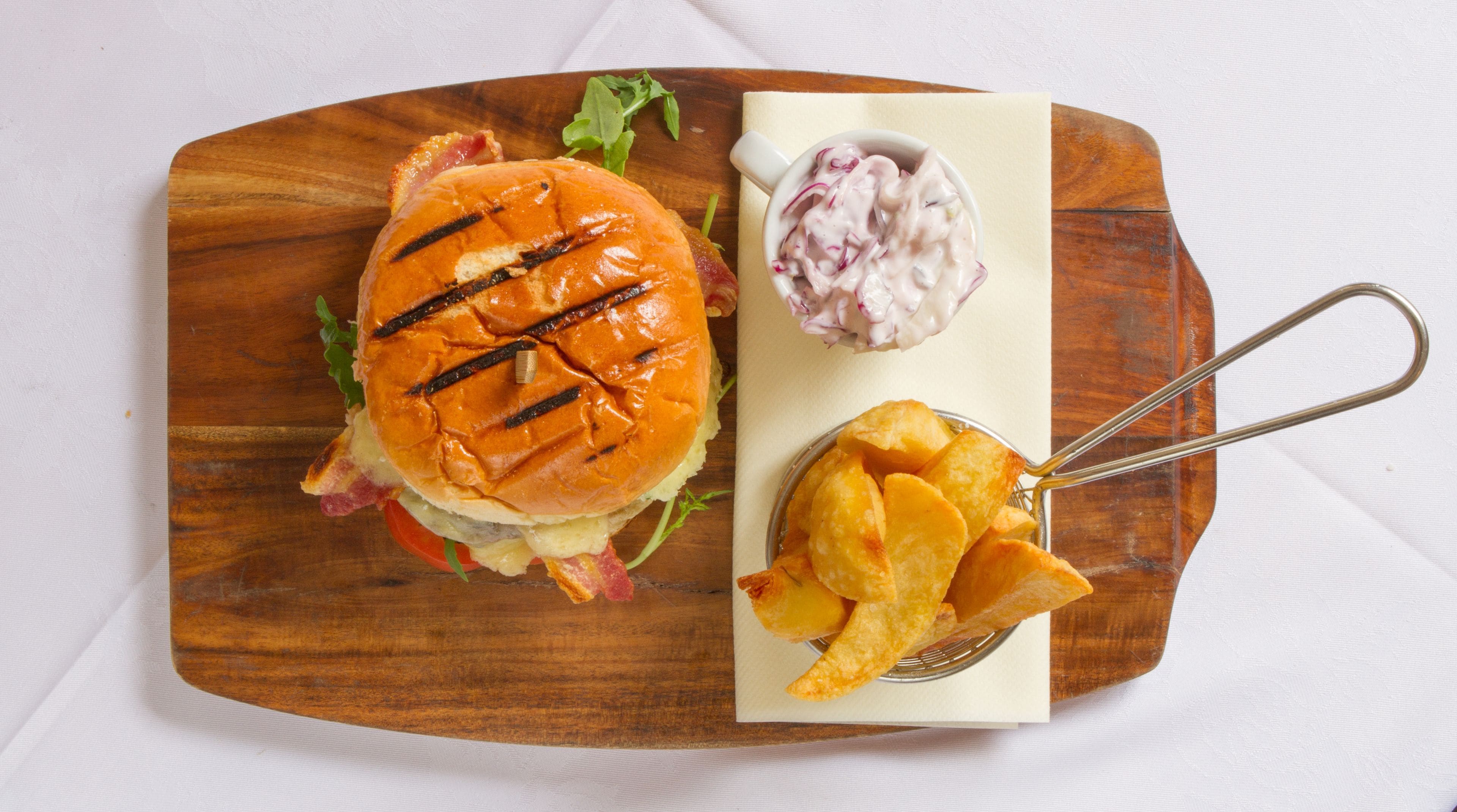 A wooden board with a grilled sandwich, coleslaw, and potato wedges.