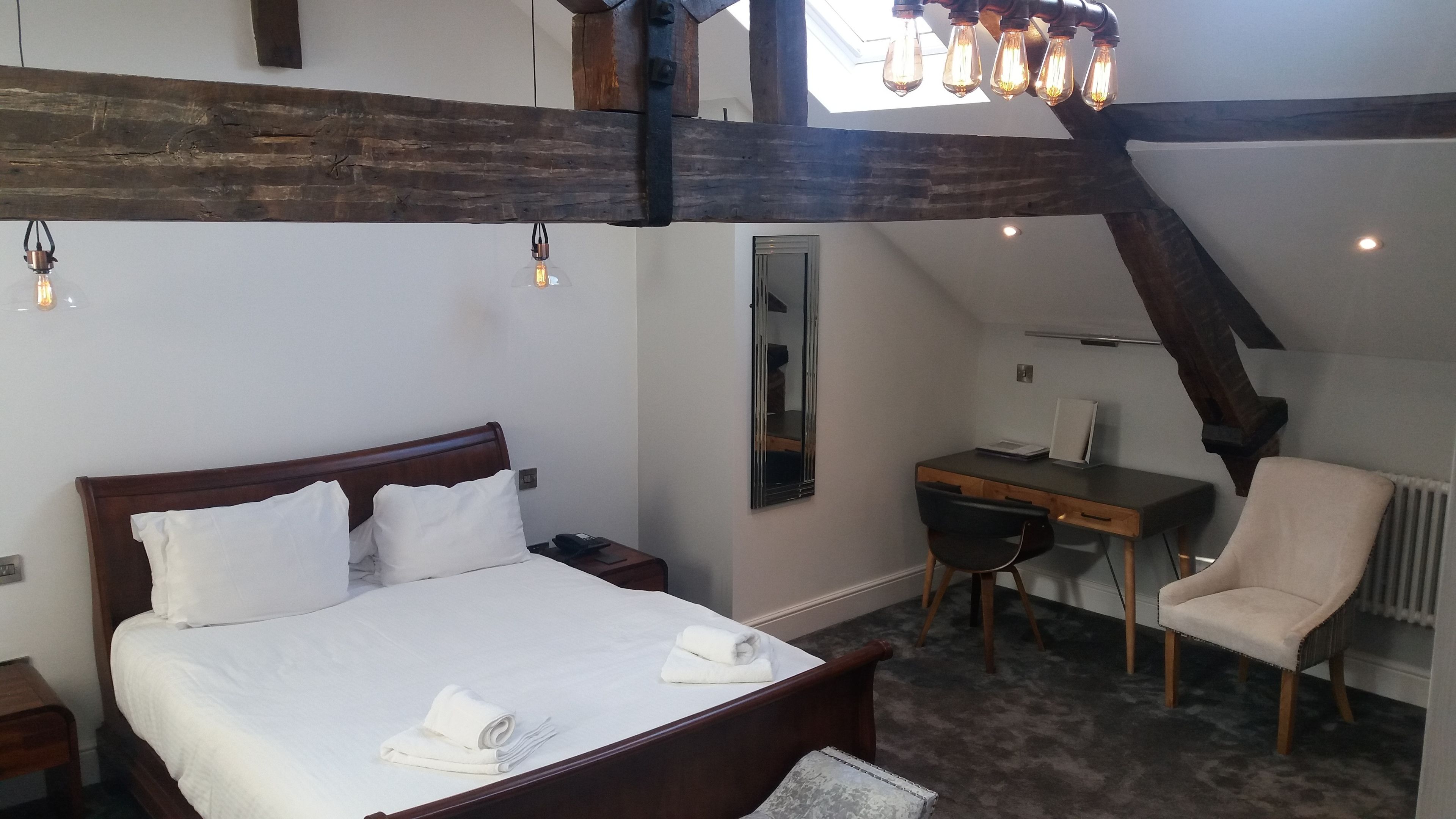Une chambre à coucher avec un lit en bois, un bureau et une chaise, agrémentée de poutres apparentes et d’une lucarne.
