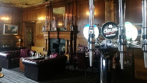 Zona de bar con chimenea, asientos de cuero y grifo de cerveza con la etiqueta 'Carling Extra Cold'.